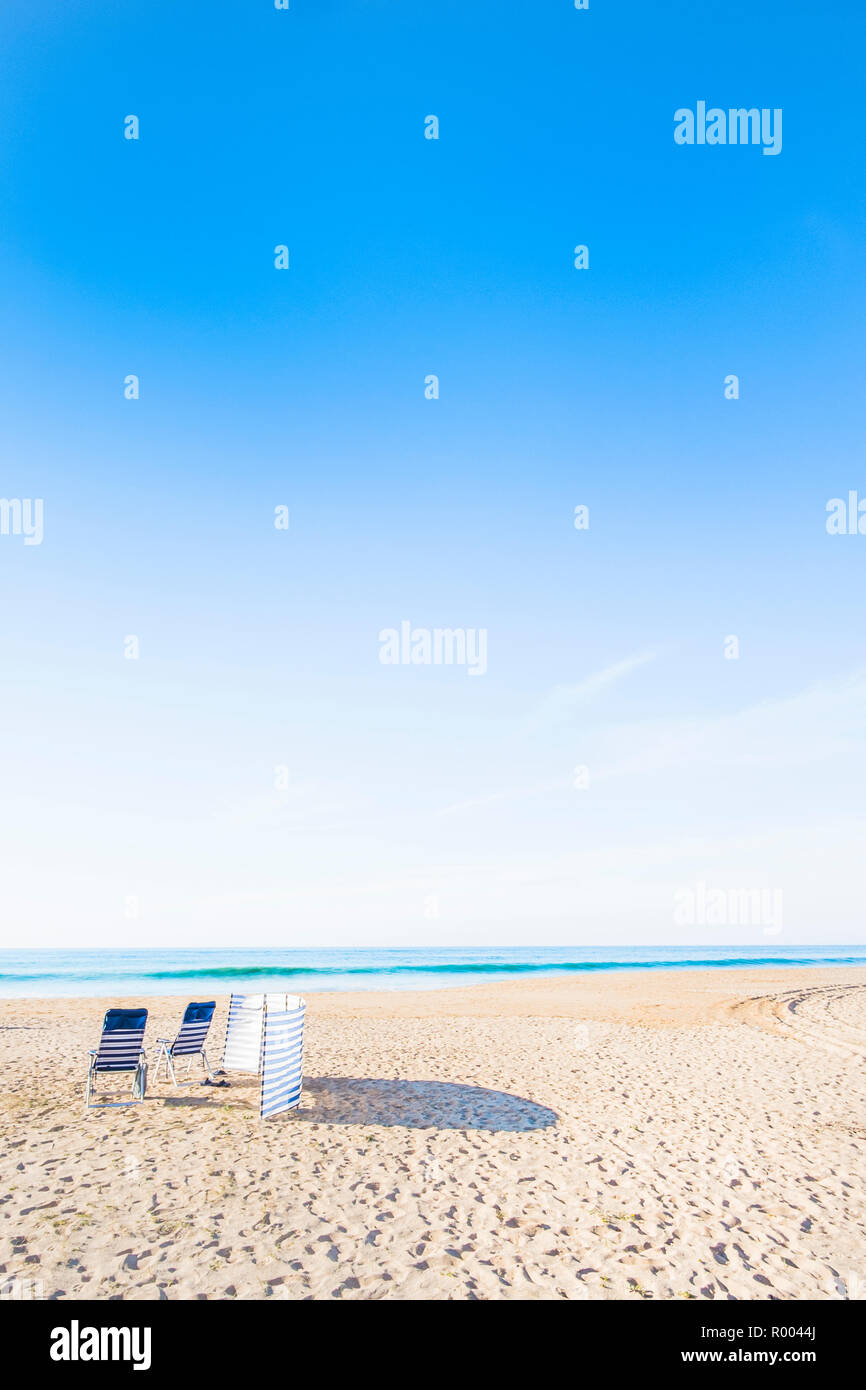 Chaises bleu et blanc et à l'abri du vent plage déserte Banque D'Images