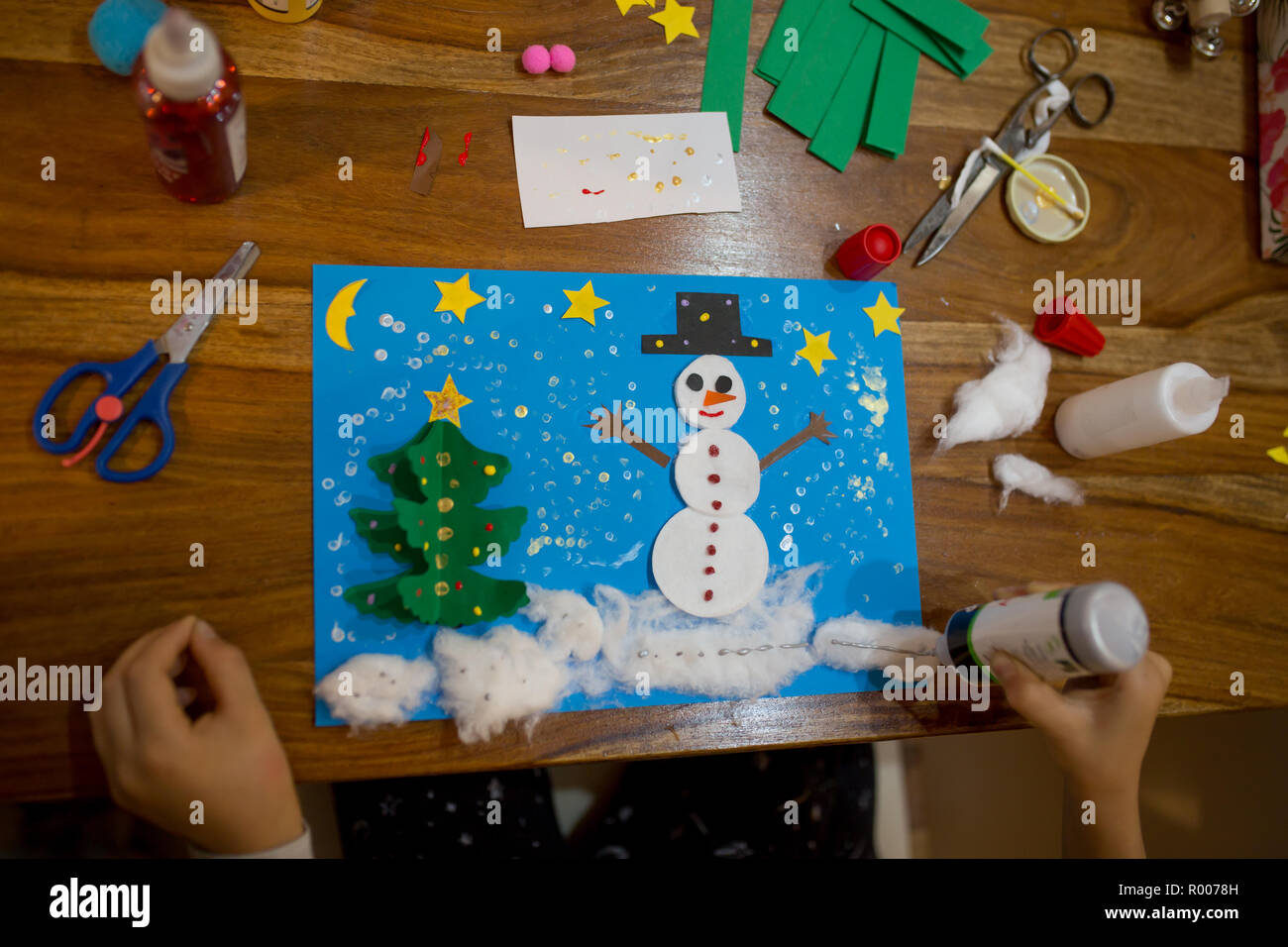 Vue de dessus de l'enfant, faisant et bonhomme hiver arbre. Bâton de colle, ciseaux, crayon, marqueurs, feuilles de papier et bouts sur fond de bois. Amusant pour les enfants wifi Banque D'Images