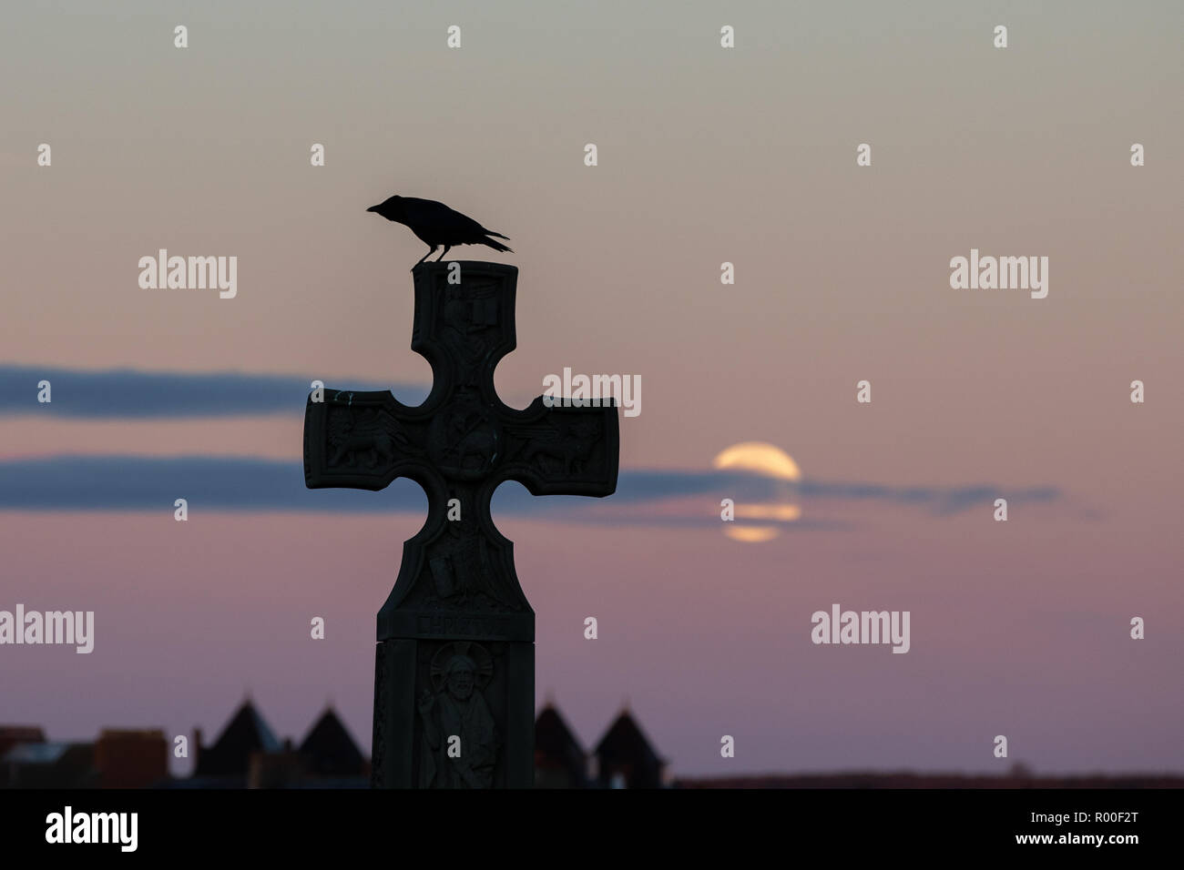 Whitby, Yorkshire, UK : 25 octobre 2018. La pleine lune se couche sur le cimetière comme un corbeau se trouve sur une croix sur Whitby Banque D'Images