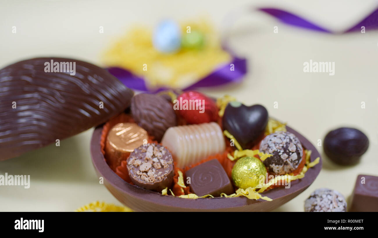 Close up composition avec la moitié de l'Ester oeuf en chocolat foncé plein de chocolats à la main Banque D'Images