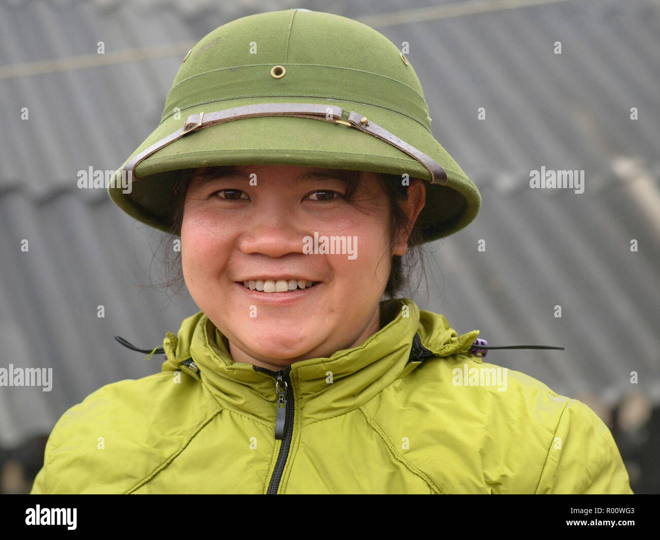 Full-figuré, jeune Vietnamien femme sourit et porte un livre vert de l'armée du Nord Vietnam pith helmet. Banque D'Images