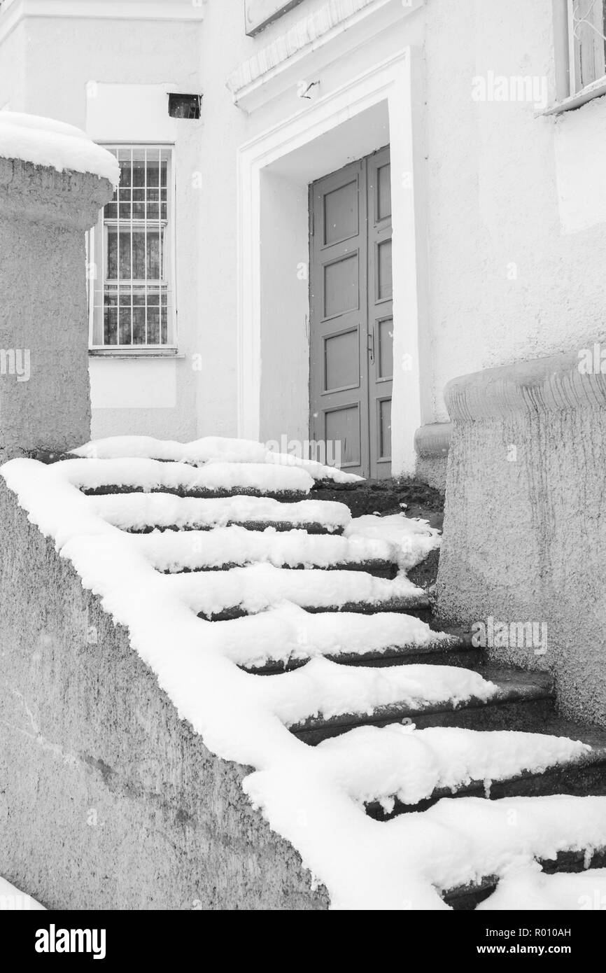 Escalier en pierre couverte de neige d'un vieil immeuble gris avec porte fermée. Banque D'Images