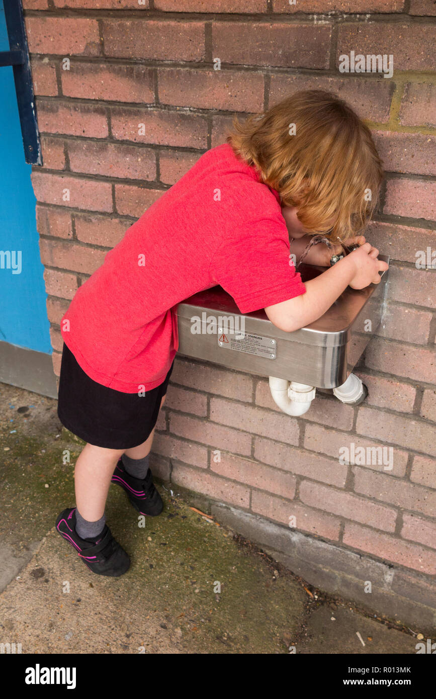 Une fillette de quatre ans à l'école Fontaine d'eau potable à partir d'un mur à l'extérieur de l'école et dans l'aire de jeux. Royaume-uni (103) Banque D'Images