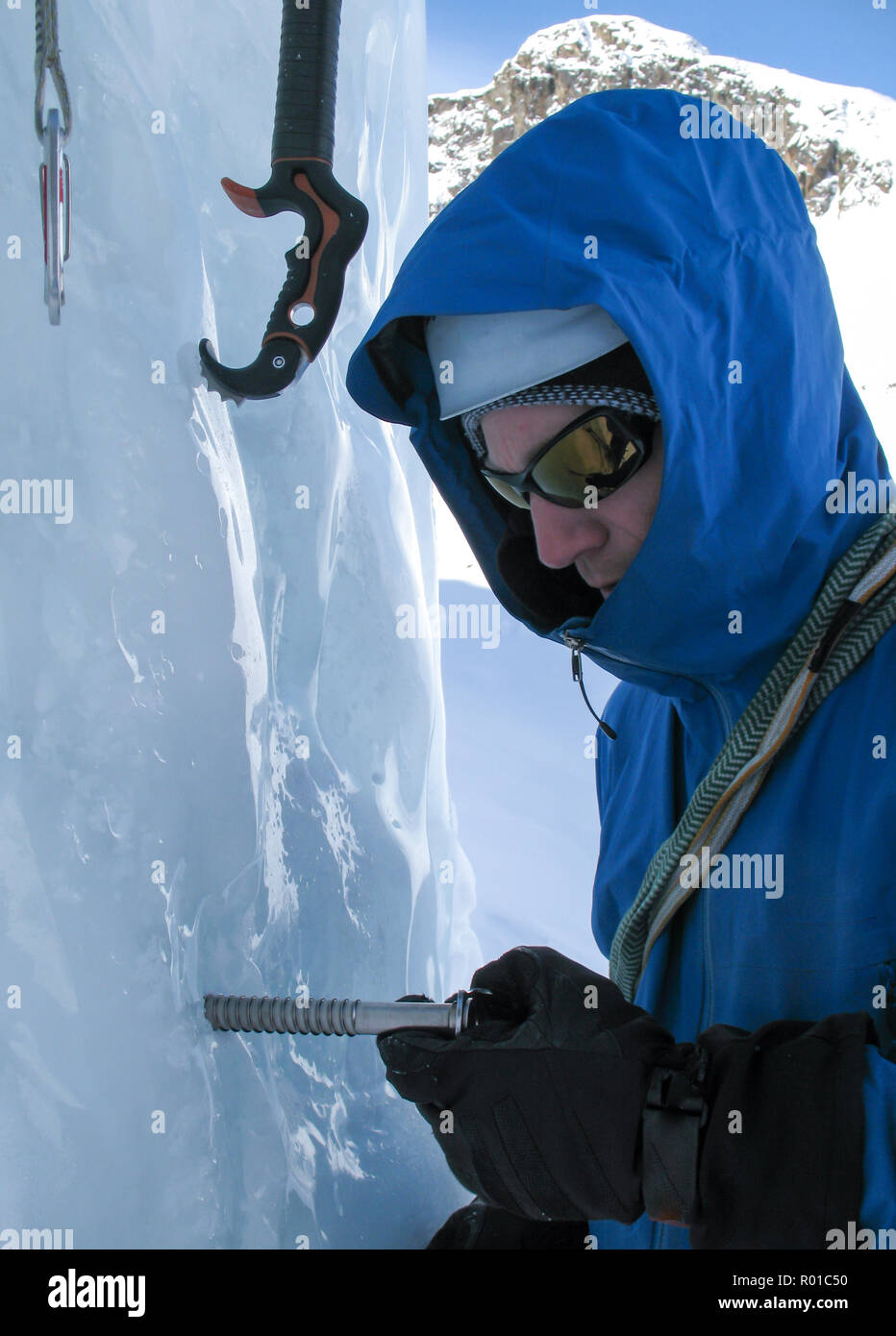 Grimpeur sur glace dans une veste bleue en tournant une vis dans une cascade de glace sur une ascension dans les Alpes de Suisse Banque D'Images