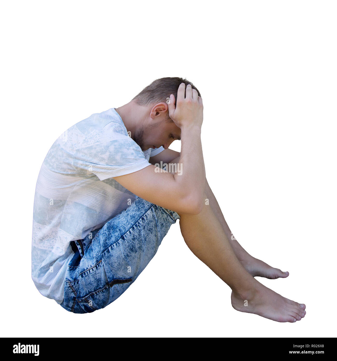 Side view full length portrait de jeune homme sadl assis sur le sol bouleversé à la recherche vers le bas et méditer plus isolé sur fond blanc. Banque D'Images