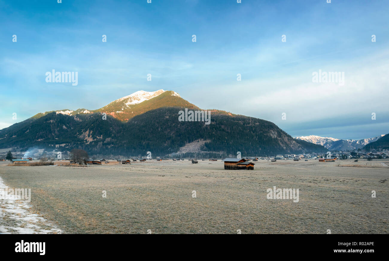 Les Alpes autrichiennes, montagnes, un village, et dispersés sur une prairie avec granges herbe gelée, près de Ehrwald, Autriche, en hiver. Banque D'Images