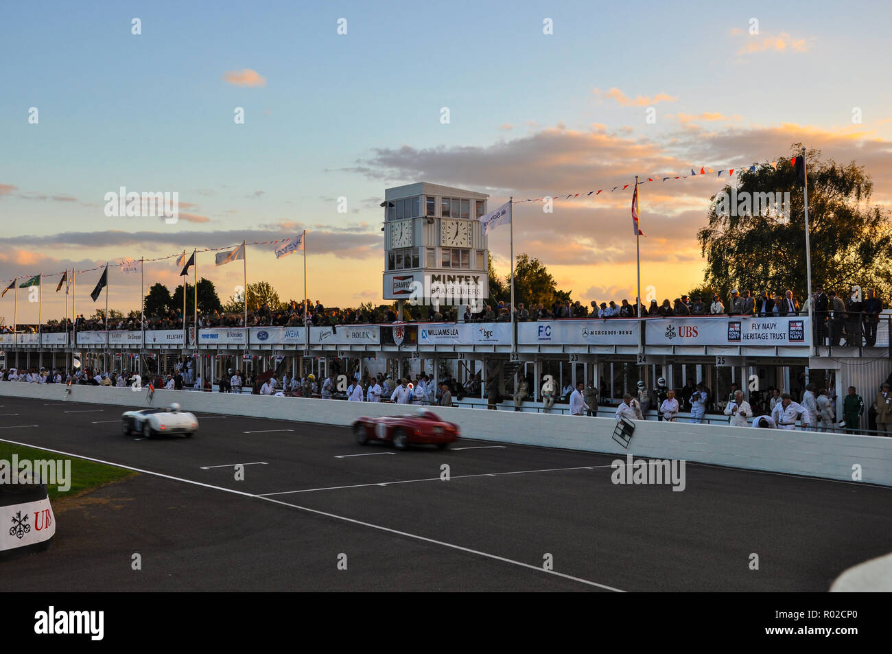 Sunset soir crépuscule course automobile vintage au Goodwood Revival. Course de voiture d'endurance. Voitures de course en ligne droite, stands droit Banque D'Images