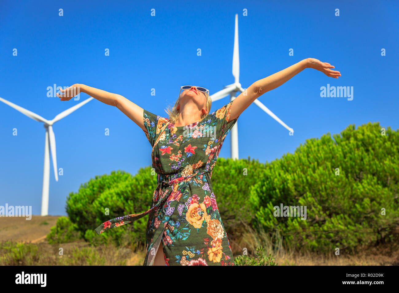 Une blonde femme heureuse à bras ouverts les éoliennes tournant en Sagres, Algarve, Portugal. L'énergie de remplacement, de l'énergie renouvelable et de la durabilité de l'environnement concept. Banque D'Images