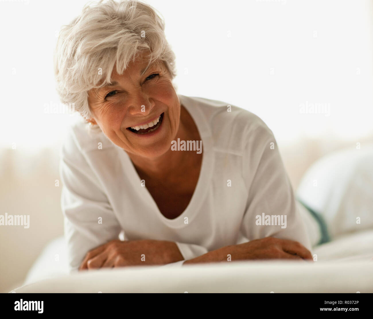 Smiling senior woman se trouve sur sur son front dans un lit. Banque D'Images