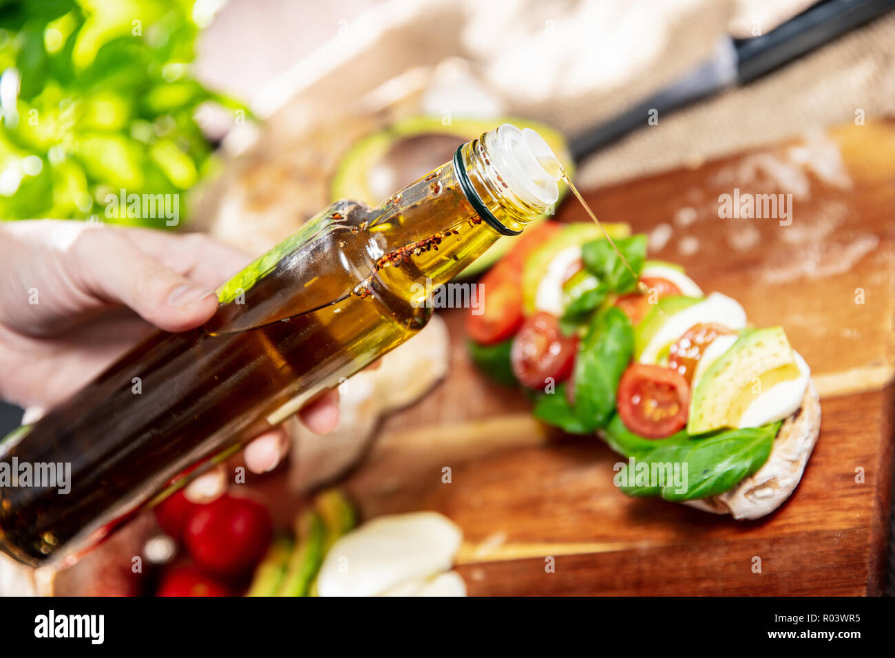 La main est de verser l'huile d'olive au basilic sur le sandwich fait de pain ciabatta, tomates, avocat, mozzarella et basilic frais. L'orientation horizontale de pho Banque D'Images