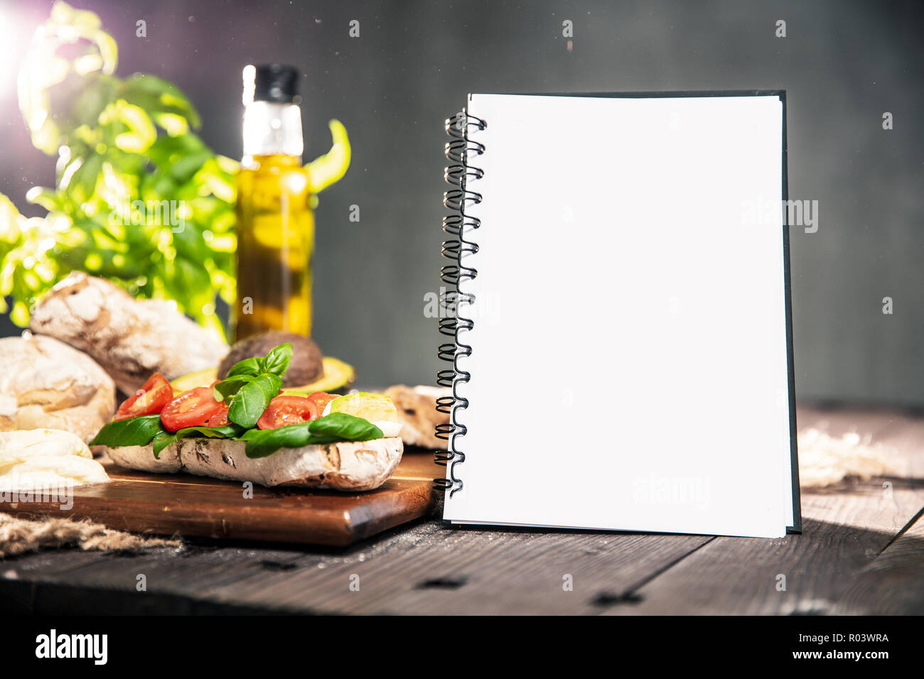 Table rustique avec du pain ciabatta, Avocat, tomates, mozzarella, huile d'olive, basilic frais et ordinateur portable avec copyspace pour votre texte. Verticall orientati Banque D'Images