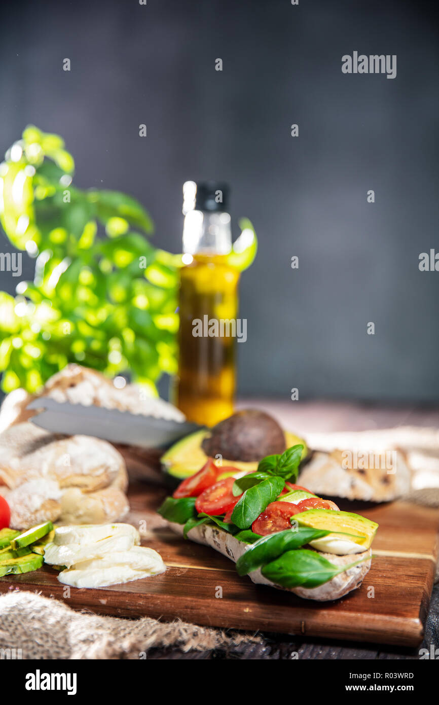 Sandwich frais de ciabatta pain, tomates, avocat, mozzarella et basilic frais sur la table rustique avec ingredietns sur l'arrière-plan. Orie verticale Banque D'Images
