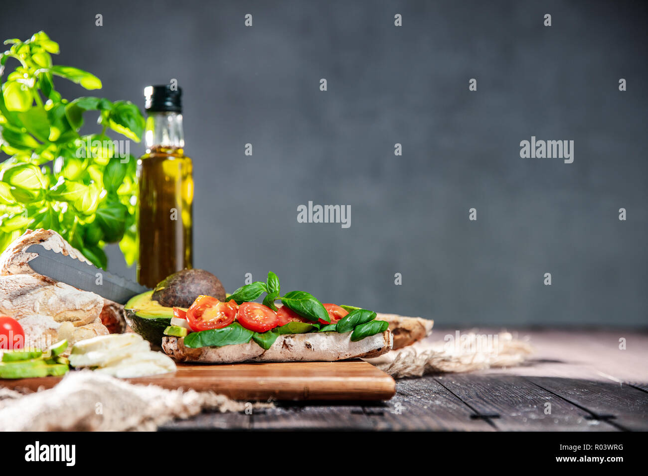 Sandwich frais de ciabatta pain, tomates, avocat, mozzarella et basilic frais sur la table rustique avec ingredietns sur l'arrière-plan. Ou horizontale Banque D'Images