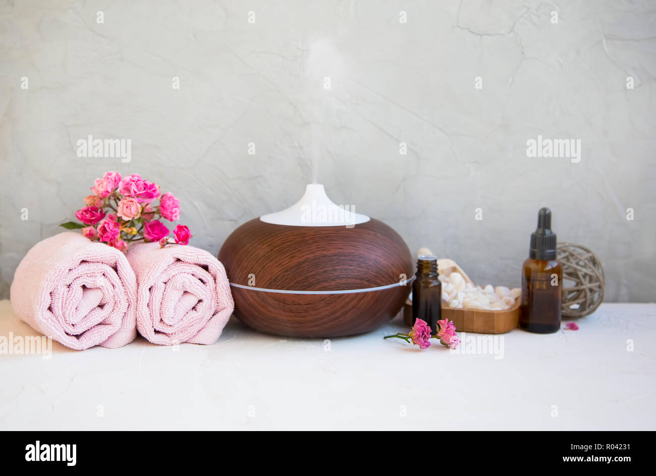 Still Life spa avec aromathérapie diffuseur, serviettes, bouteilles d'huile de rose et de sels de bain sur fond de béton Banque D'Images