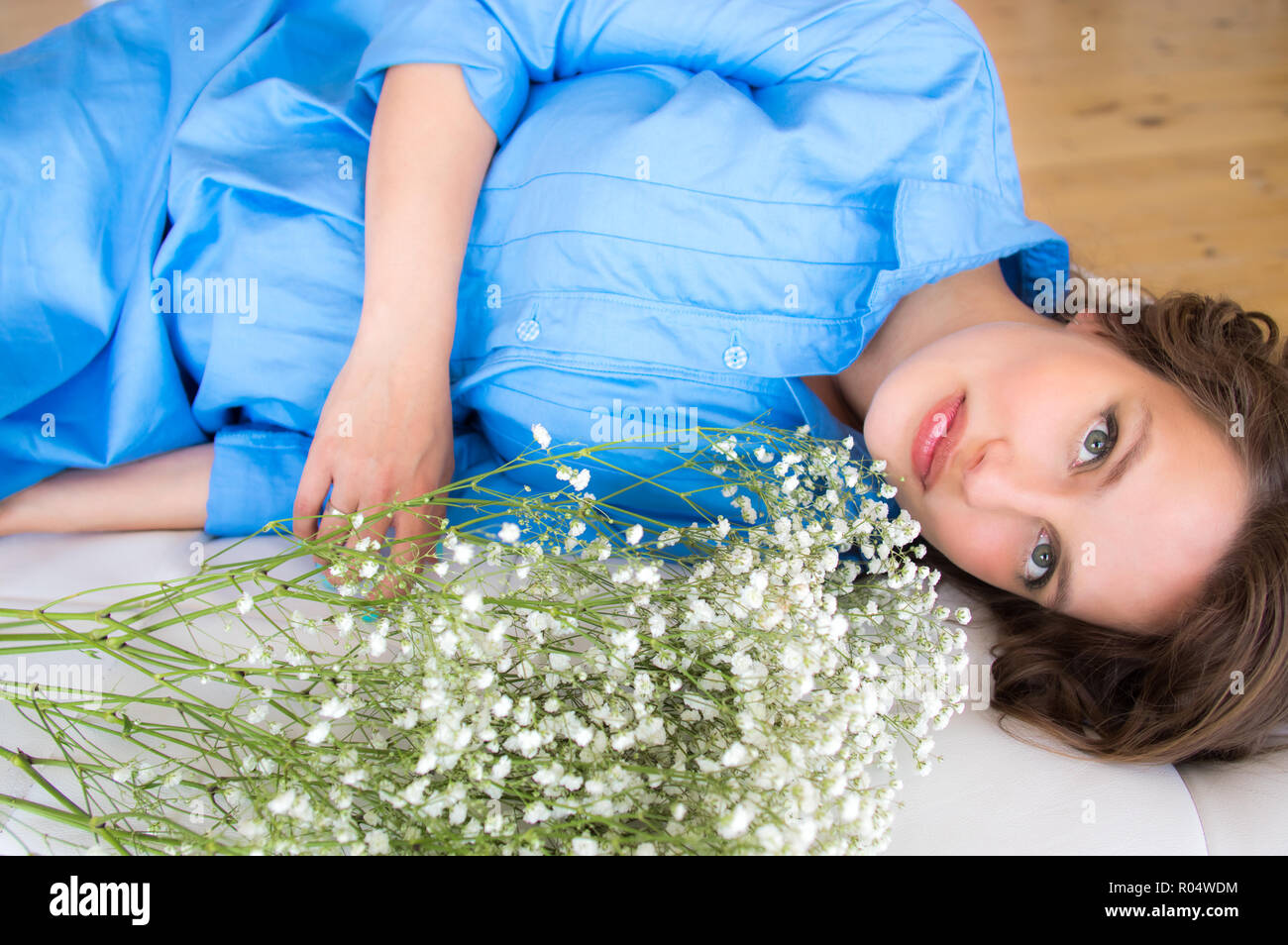 Femme enceinte en robe bleue se trouve sur canapé ronde avec bouquet de fleurs Banque D'Images