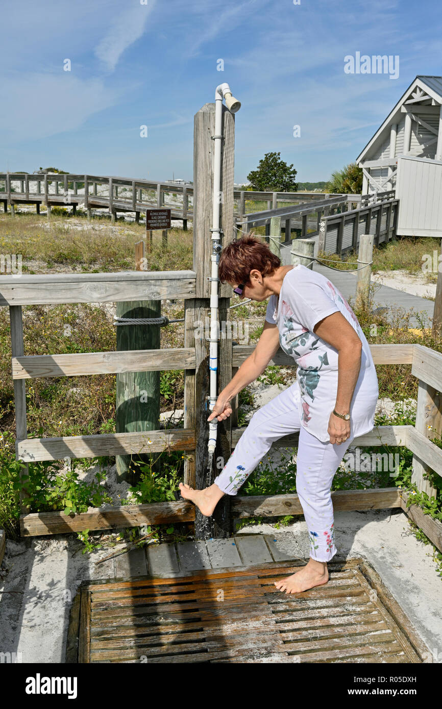 Femme senior mature lavant le sable de plage de ses pieds à une douche extérieure de plage en Floride, USA. Banque D'Images