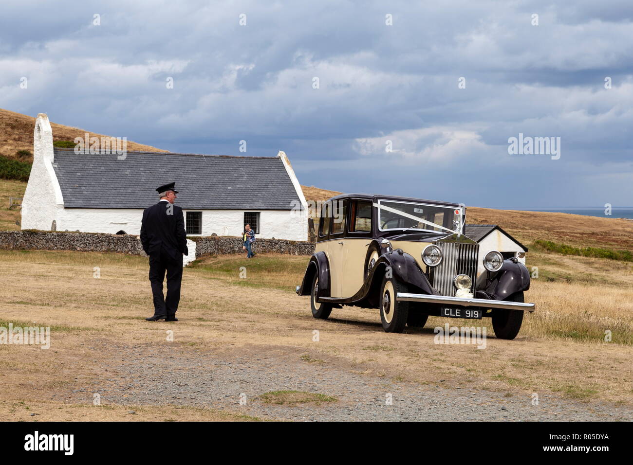 Un classique 1935 Rolls Royce 20/25 attend près de l'église Sainte Croix (Eglwys Y Grog), tandis qu'il est chauffeur stands à proximité. Ceredigion, pays de Galles, Mwnt Banque D'Images