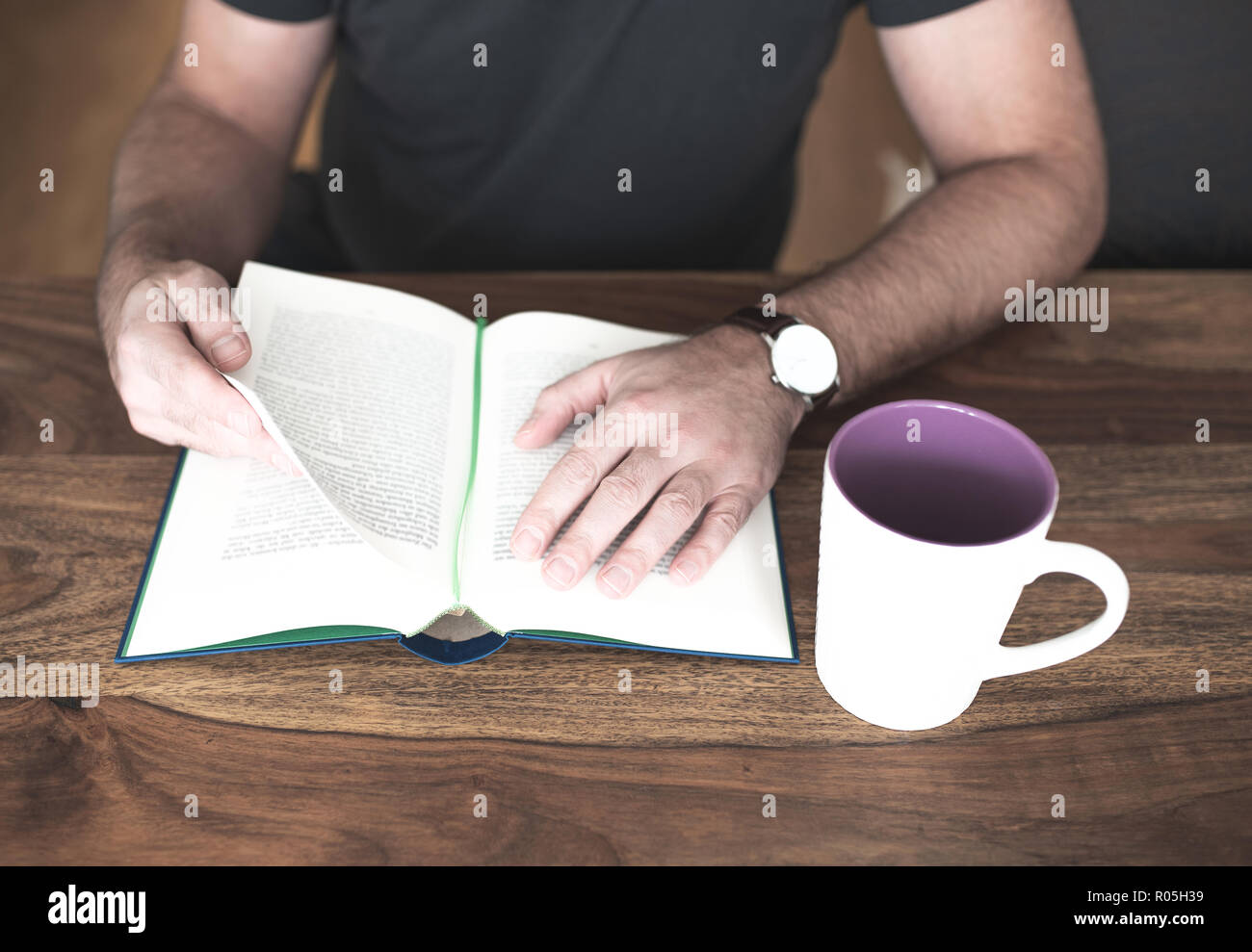 L'homme assis à table en bois de la lecture d'un livre Banque D'Images