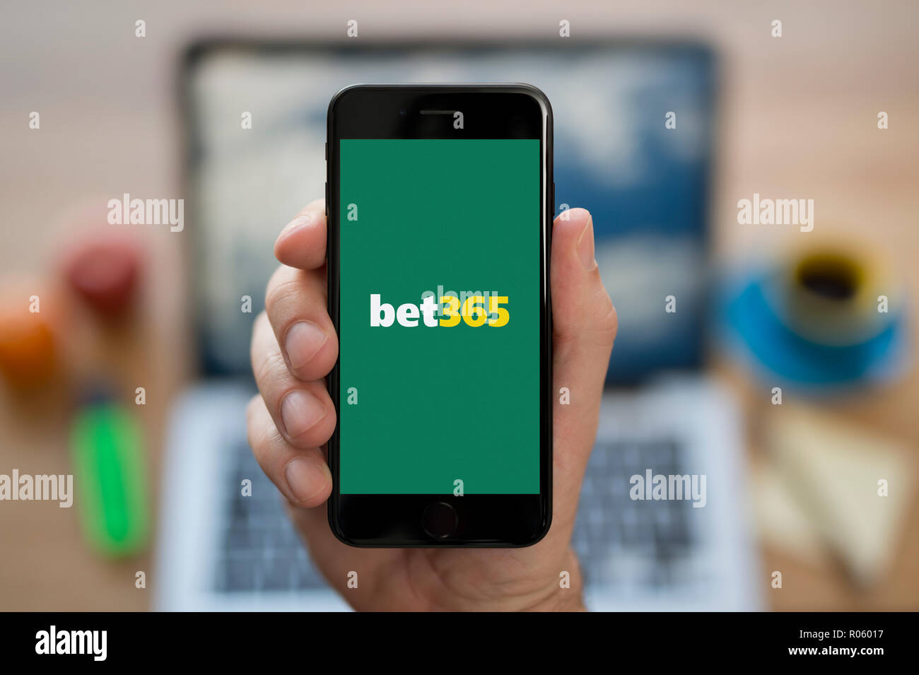 Un homme se penche sur son iPhone qui affiche le logo de bet365, alors qu'assis à son bureau de l'ordinateur (usage éditorial uniquement). Banque D'Images
