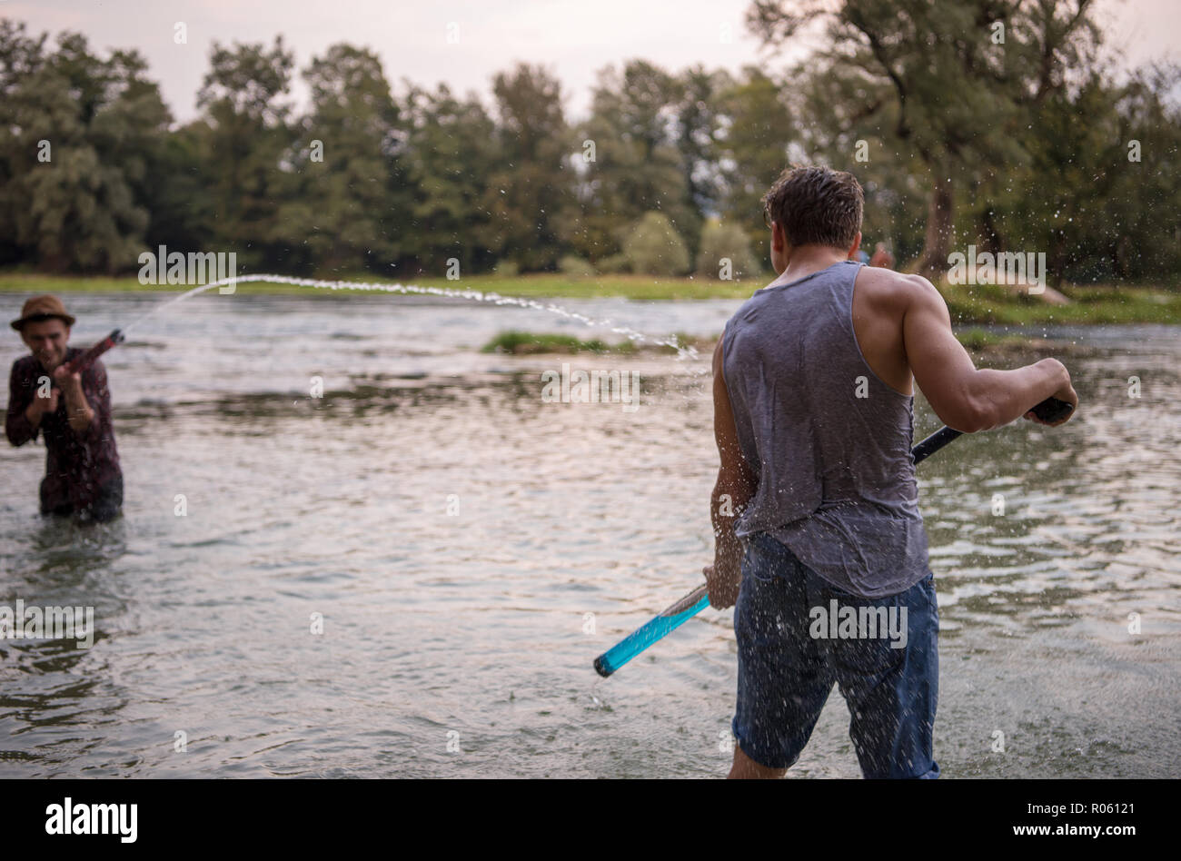 Les jeunes hommes s'amusant avec les pistolets à eau tout en éclaboussant les uns les autres pendant le coucher du soleil sur la rivière Banque D'Images