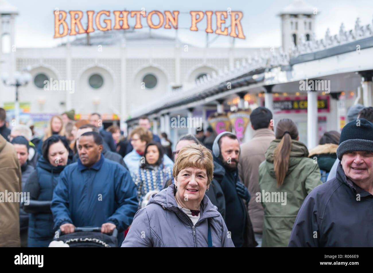 Des foules de gens portant des manteaux par une froide journée de printemps sur une longue jetée de Brighton, East Sussex, Angleterre, Royaume-Uni. Banque D'Images