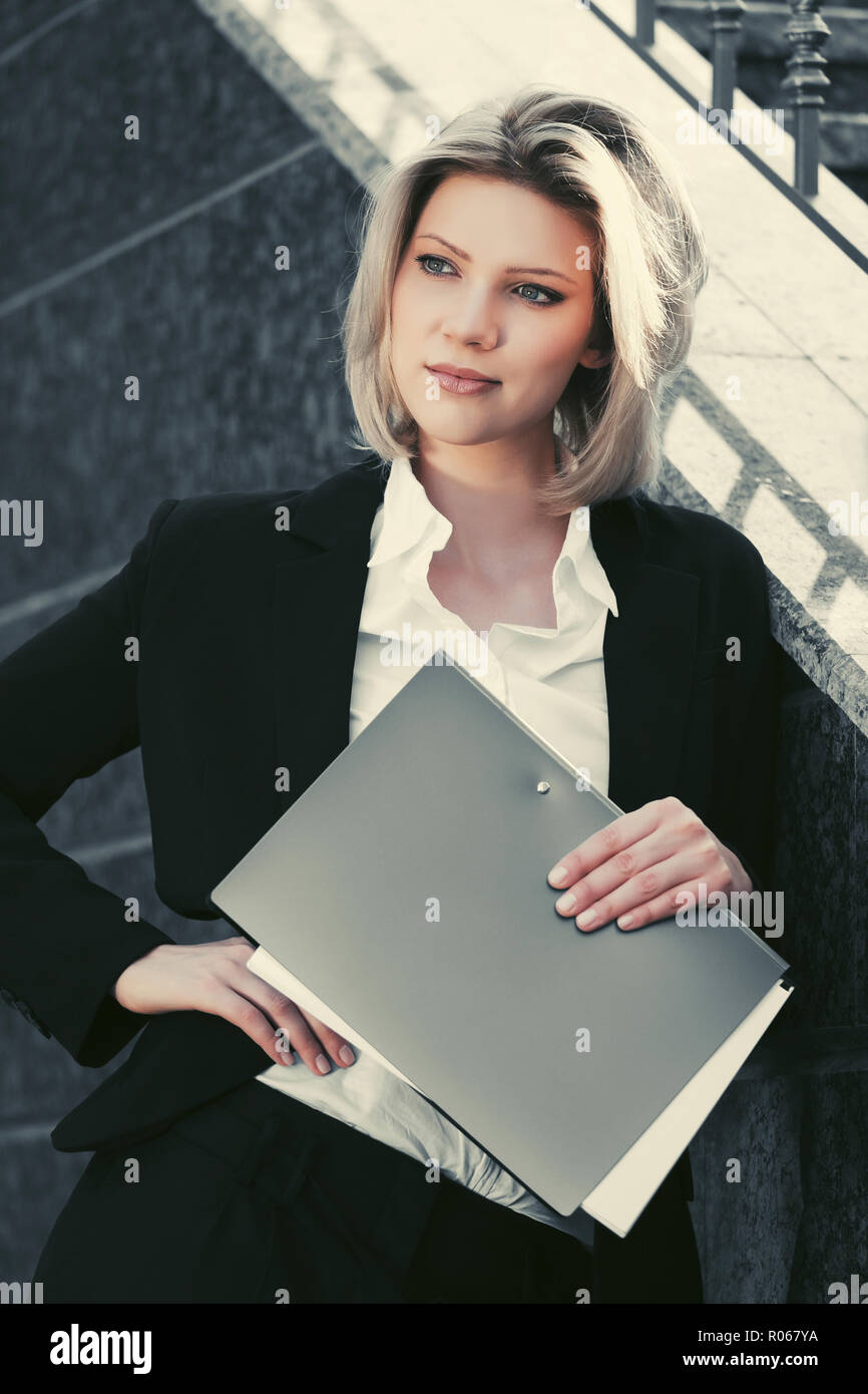 Happy young business woman avec fichier dossier à l'immeuble de bureaux. Modèle de mode élégant en costume noir outdoor Banque D'Images