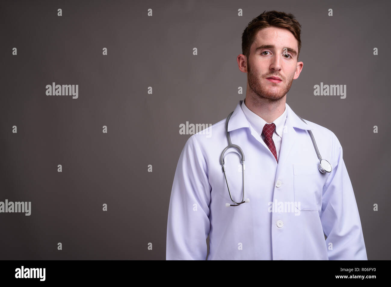 Jeune homme séduisant médecin contre l'arrière-plan gris Banque D'Images