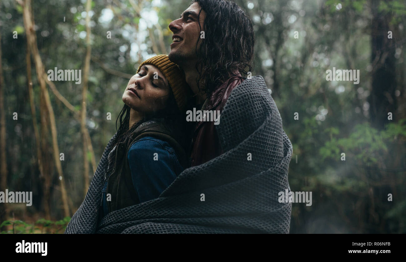 Couple romantique sous la pluie au parc. Homme debout derrière femme sous la pluie, à la fois enveloppé dans une couverture de forest. Banque D'Images