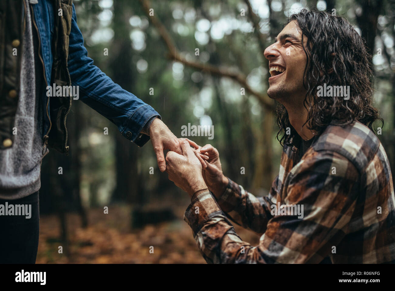 Smiling young man putting bague de fiançailles sur la main de femme à l'extérieur sous la pluie. Cheerful guy faire proposition de mariage de petite amie à parc. Banque D'Images