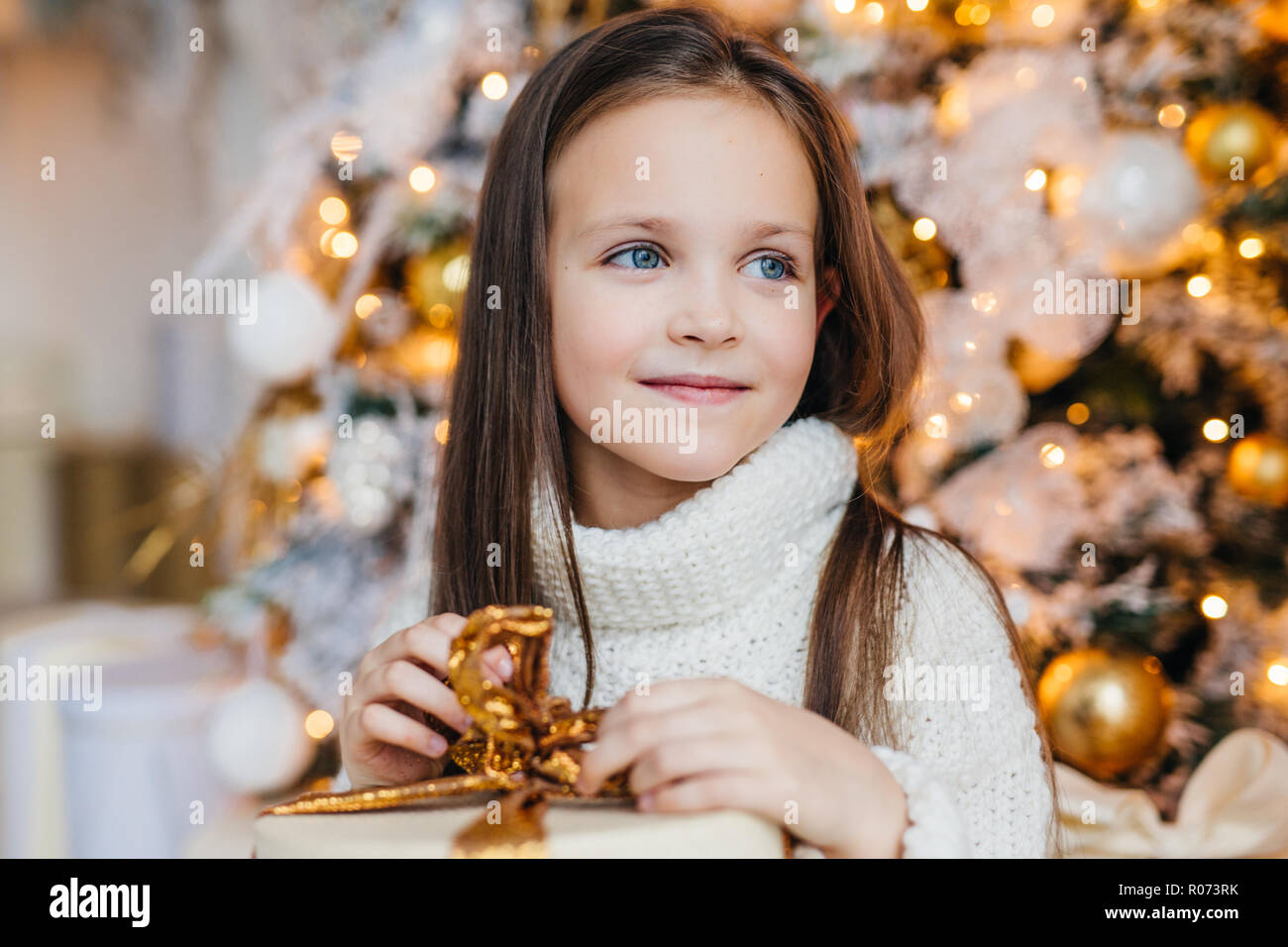 Adorable Petite Fille Avec Des Yeux Bleus De Longs Cheveux Noirs Porte Blanc Chaud Tricote Chandail Detient Actuellement Contre Decore Nouvelle Annee Tr Photo Stock Alamy