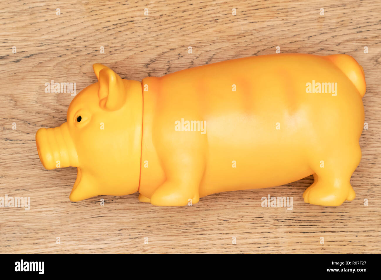 Grand jouet en caoutchouc jaune - un cochon couché sur une table en bois Banque D'Images