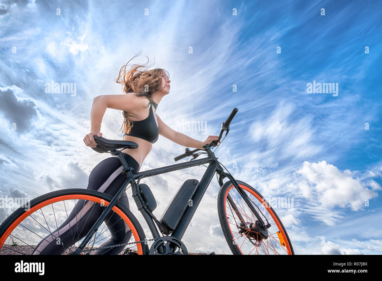 Athletic Girl avec cheveux au vent des vélo électrique. Portrait en extérieur contre blue cloudy sky Banque D'Images