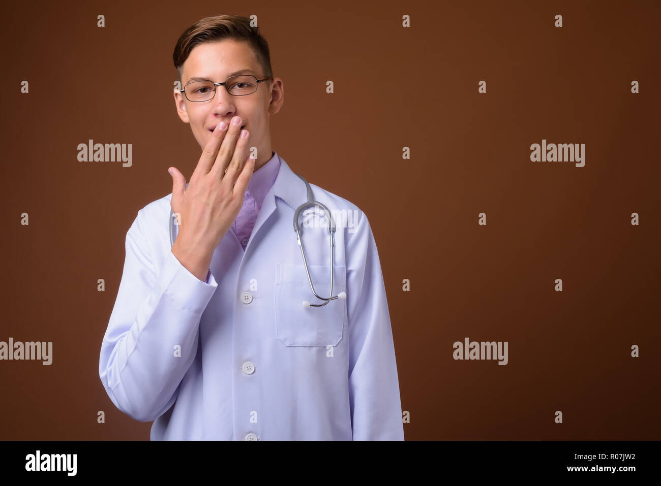 Studio shot of young handsome médecin contre fond brun Banque D'Images