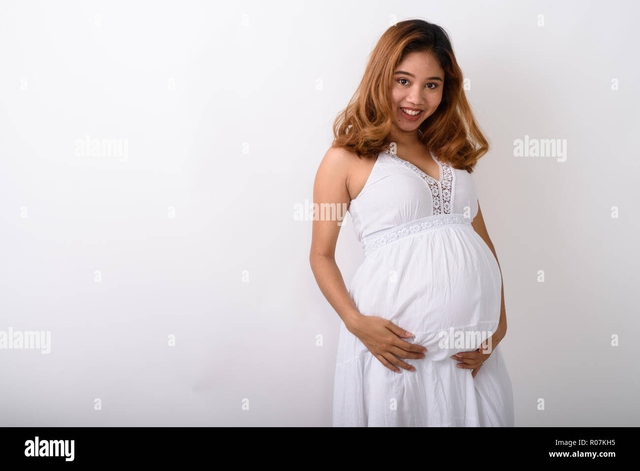 Studio shot of young happy pregnant woman smiling contre l'Asiatique Banque D'Images