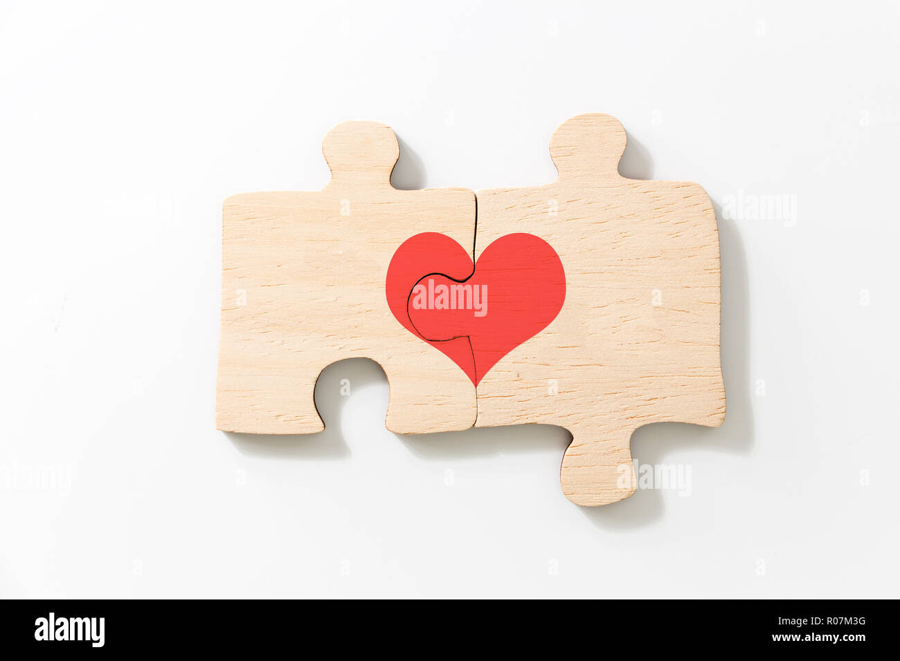 Deux pièces jointes de puzzle en bois, avec cœur rouge, sur fond blanc. Banque D'Images