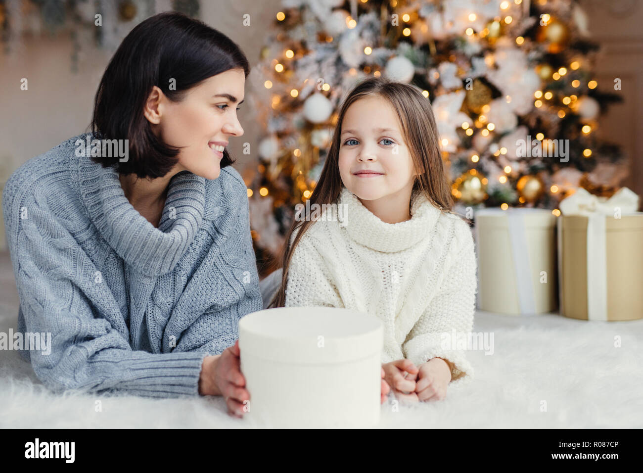 Célébration de l'hiver et concept. Jolie jolie petite fille aux yeux bleus en blanc en tricot et pull femme brunette ont bon repos à la maison, passent Banque D'Images