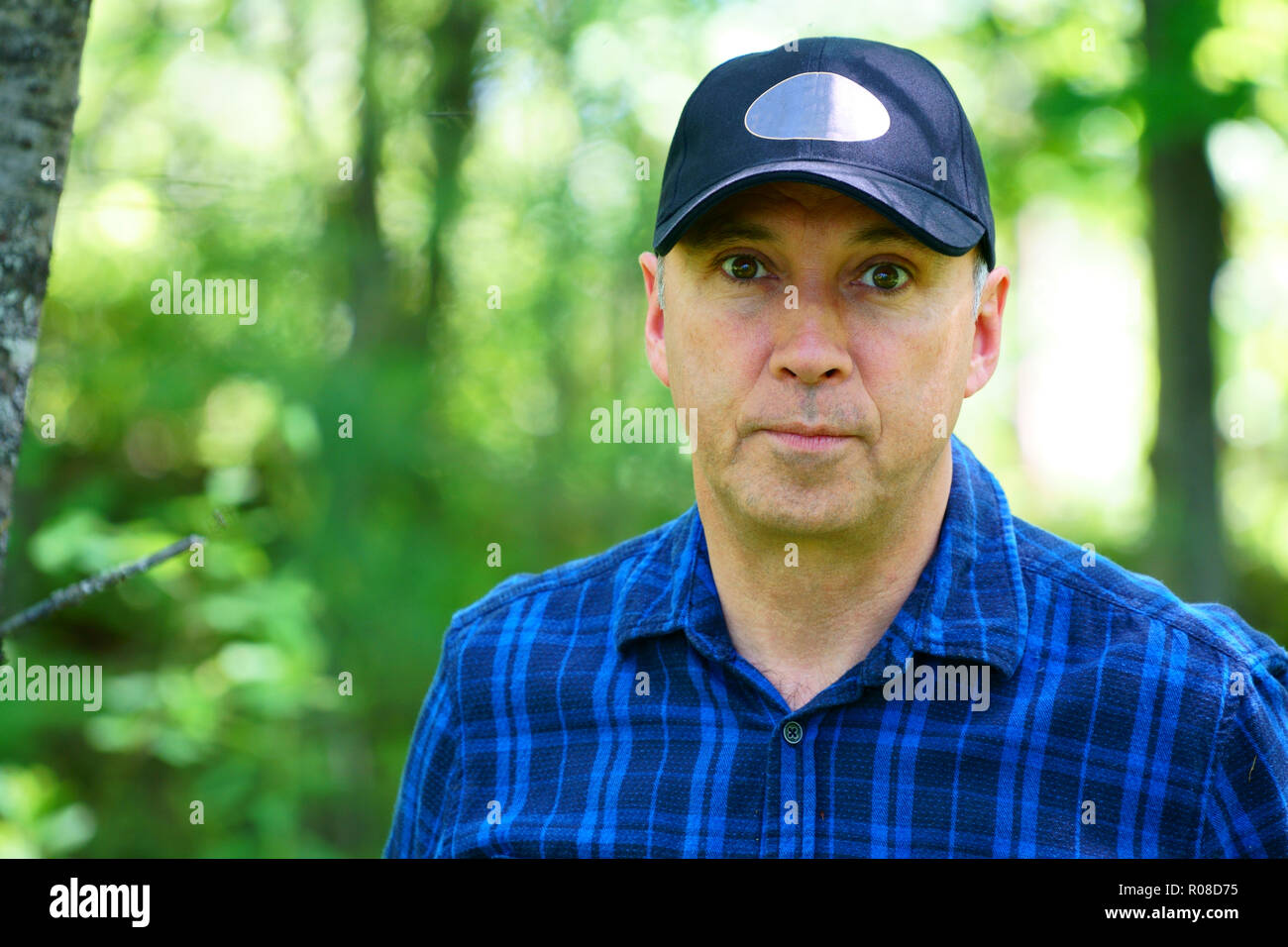 Portrait d'un homme sérieux est à la recherche dans l'appareil photo pour un portrait lors d'une randonnée dans la forêt portant une chemise à carreaux bleu et un chapeau noir. Banque D'Images