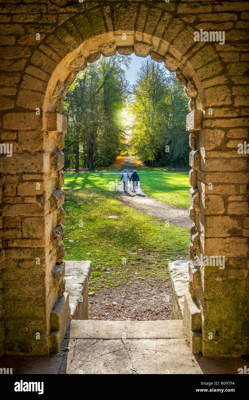 Un couple marche main dans la main dans le soleil d'automne dans le parc de Cirencester, Gloucestershire. Banque D'Images