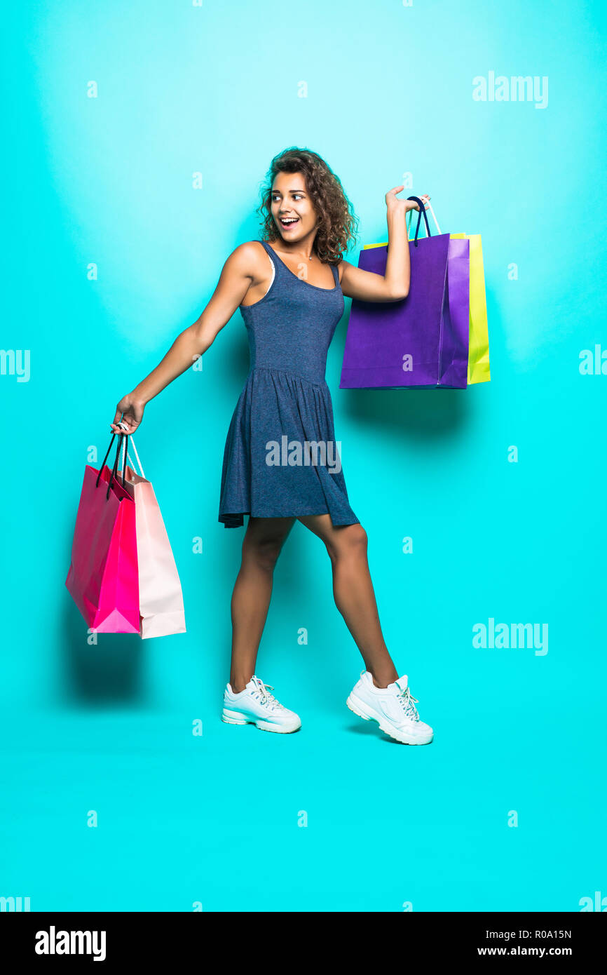 Portrait jolie femme latine en tenue d'été, chapeau de paille, lunettes de garder les paquets de sacs contenant les achats effectués après shopping isolé sur fond bleu Banque D'Images