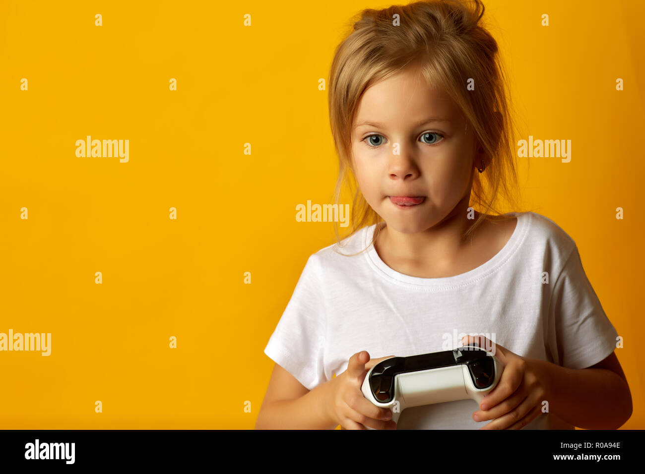 Peu absorbé girl in white t-shirt holding manette de jeu jouer jeu vidéo sur fond jaune Banque D'Images