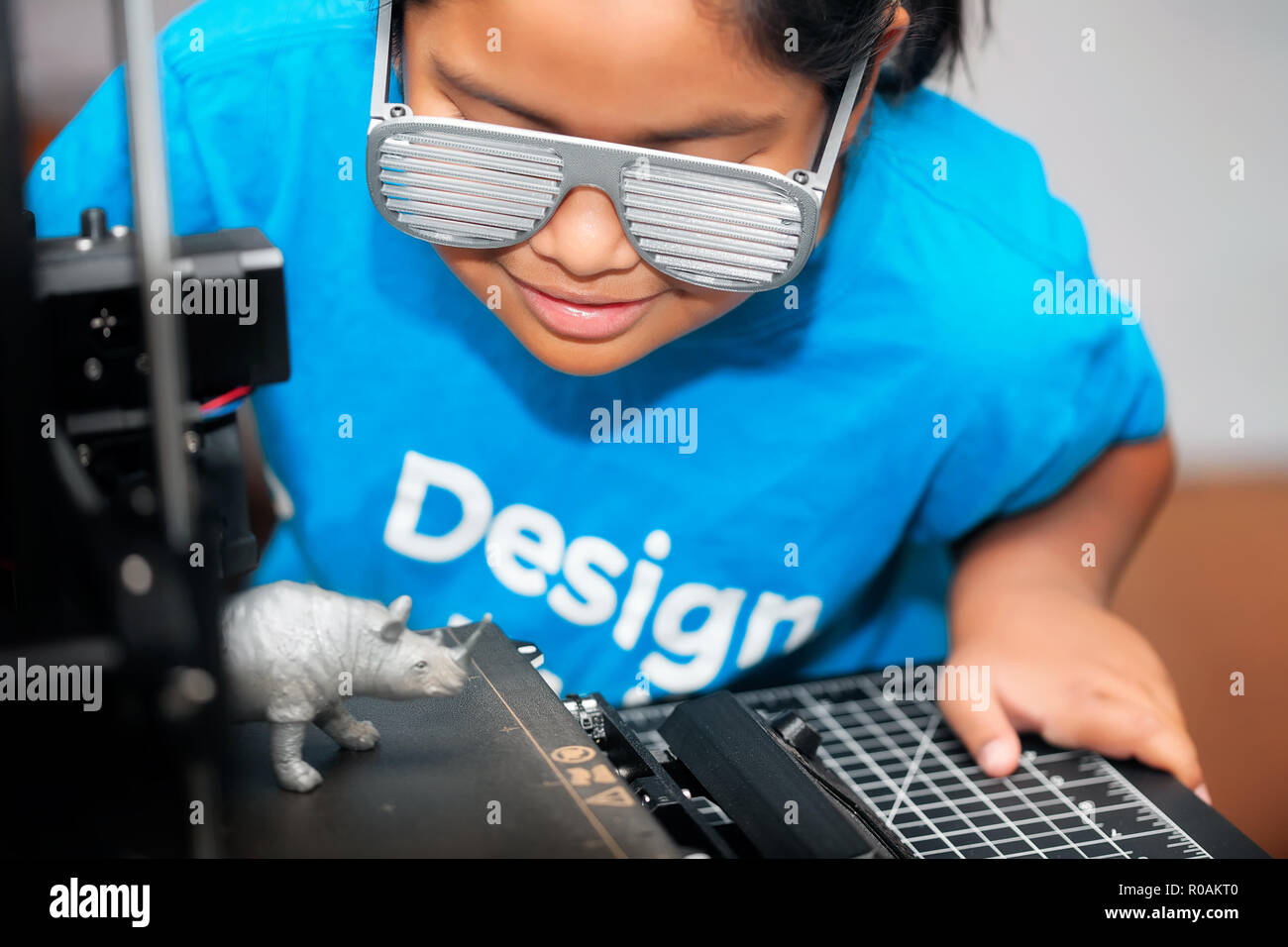 Un jeune fille de race mixte, portant une chemise qui dit design, est donnant sur la 3d impression d'un rhinocéros gris pour sa classe de la tige. Banque D'Images
