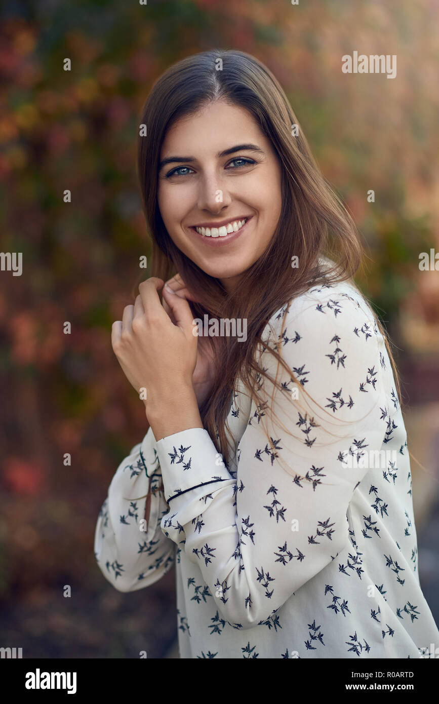 Belle jeune femme dans une rue ou l'automne automne coloré debout sur le côté pour l'appareil photo avec sa main sur sa joue en souriant à l'appareil photo Banque D'Images