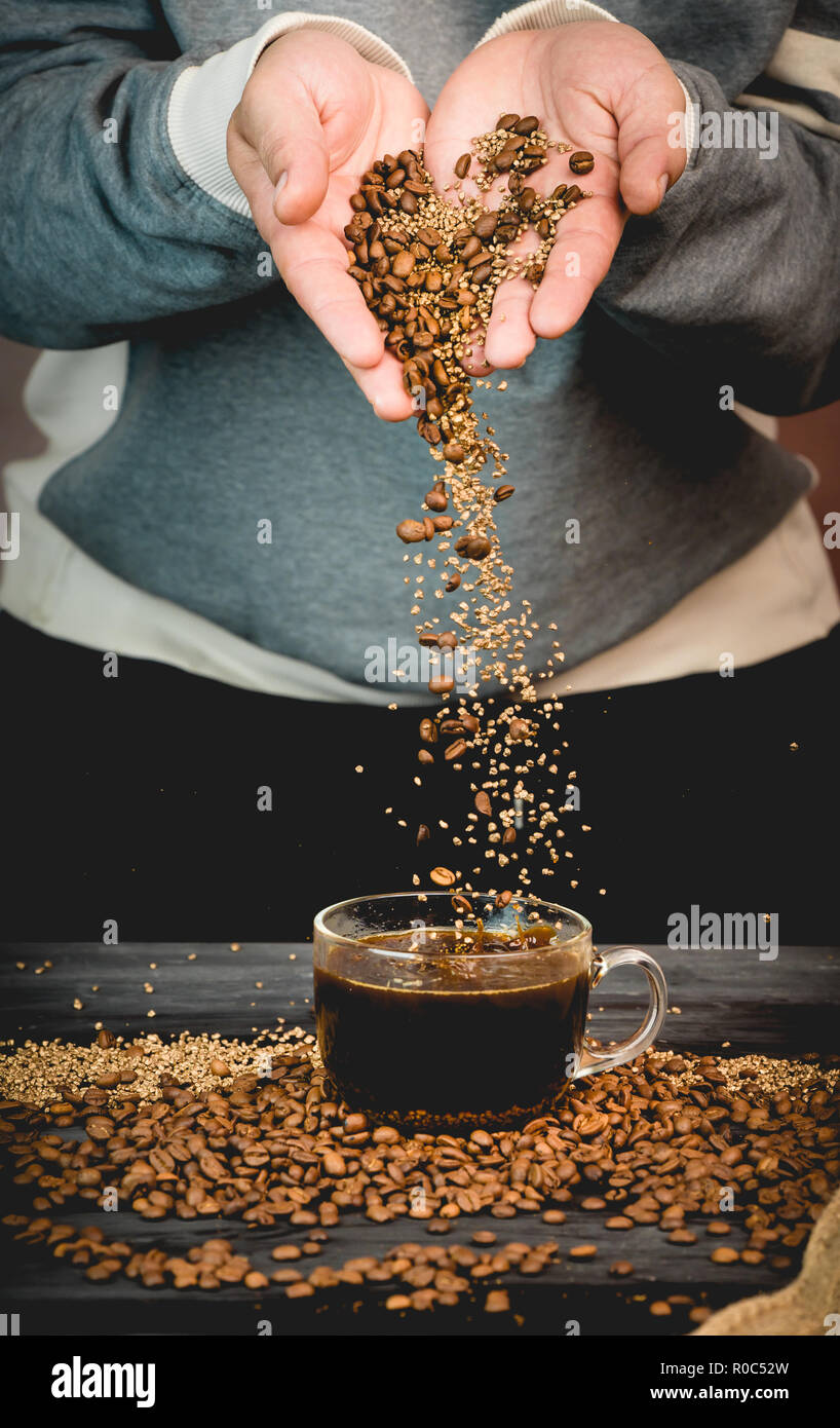 Les grains de café et le café instantané se déverse vers le bas directement à partir de la main dans une tasse de café fraîchement moulu Banque D'Images