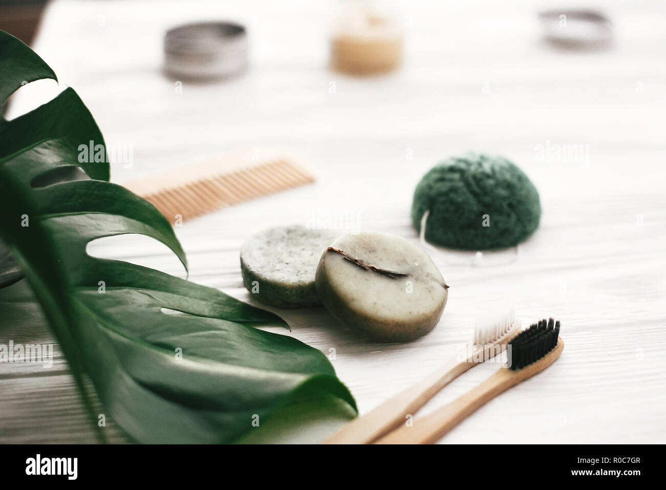 Eco friendly bambou naturel brosses à dents, dentifrice, shampoing bar en verre, brosse en bois et bois blanc sur éponge konjaku avec feuilles vert monstera. Banque D'Images