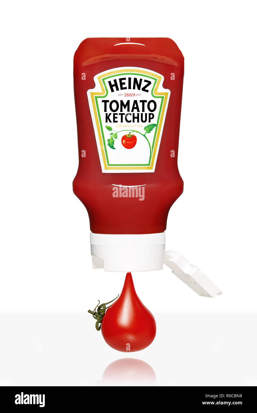 Tomate cerise qui s'écoule de la bouteille de ketchup Heinz isolé sur fond blanc. Banque D'Images