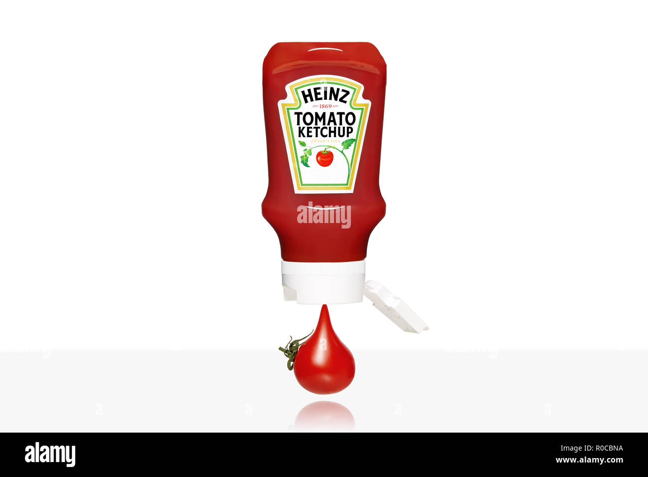 Tomate cerise qui s'écoule de la bouteille de ketchup Heinz isolé sur fond blanc. Banque D'Images
