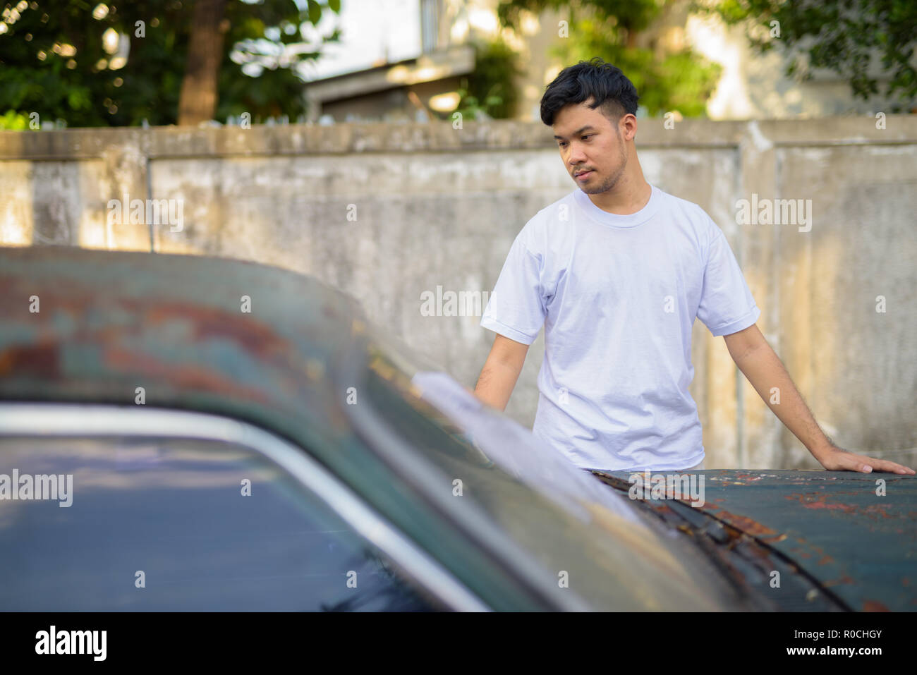 Young Asian man avec vieille voiture rouillée dans les rues à l'extérieur Banque D'Images