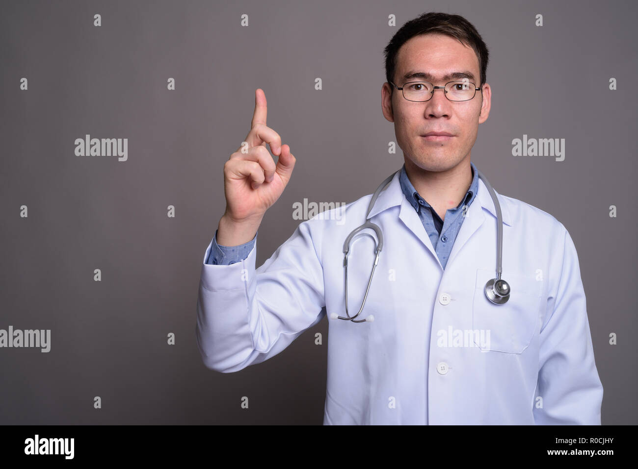 Young Asian man médecin contre l'arrière-plan gris Banque D'Images