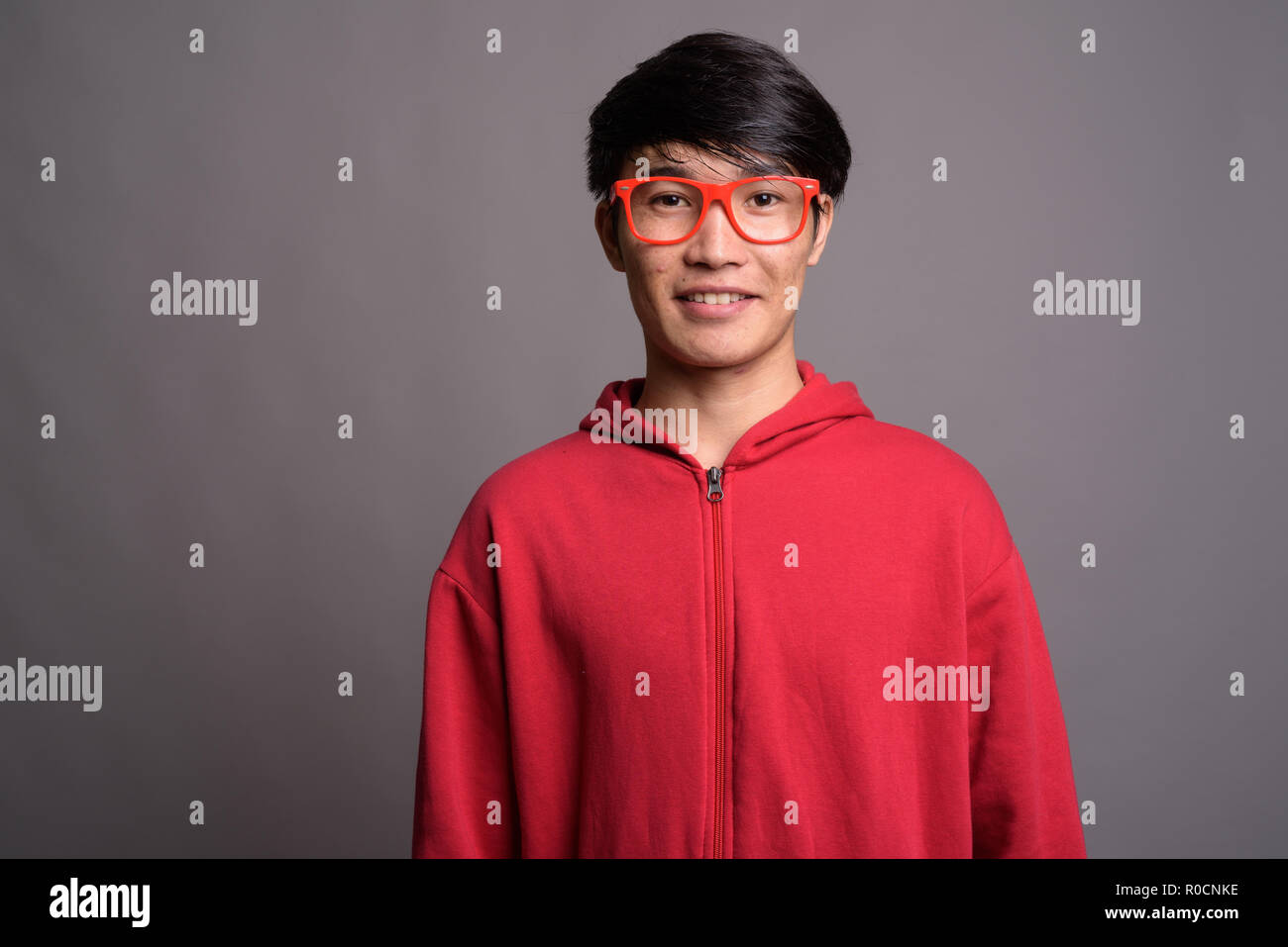 Young Asian man wearing red jacket avec lunettes contre gray Banque D'Images