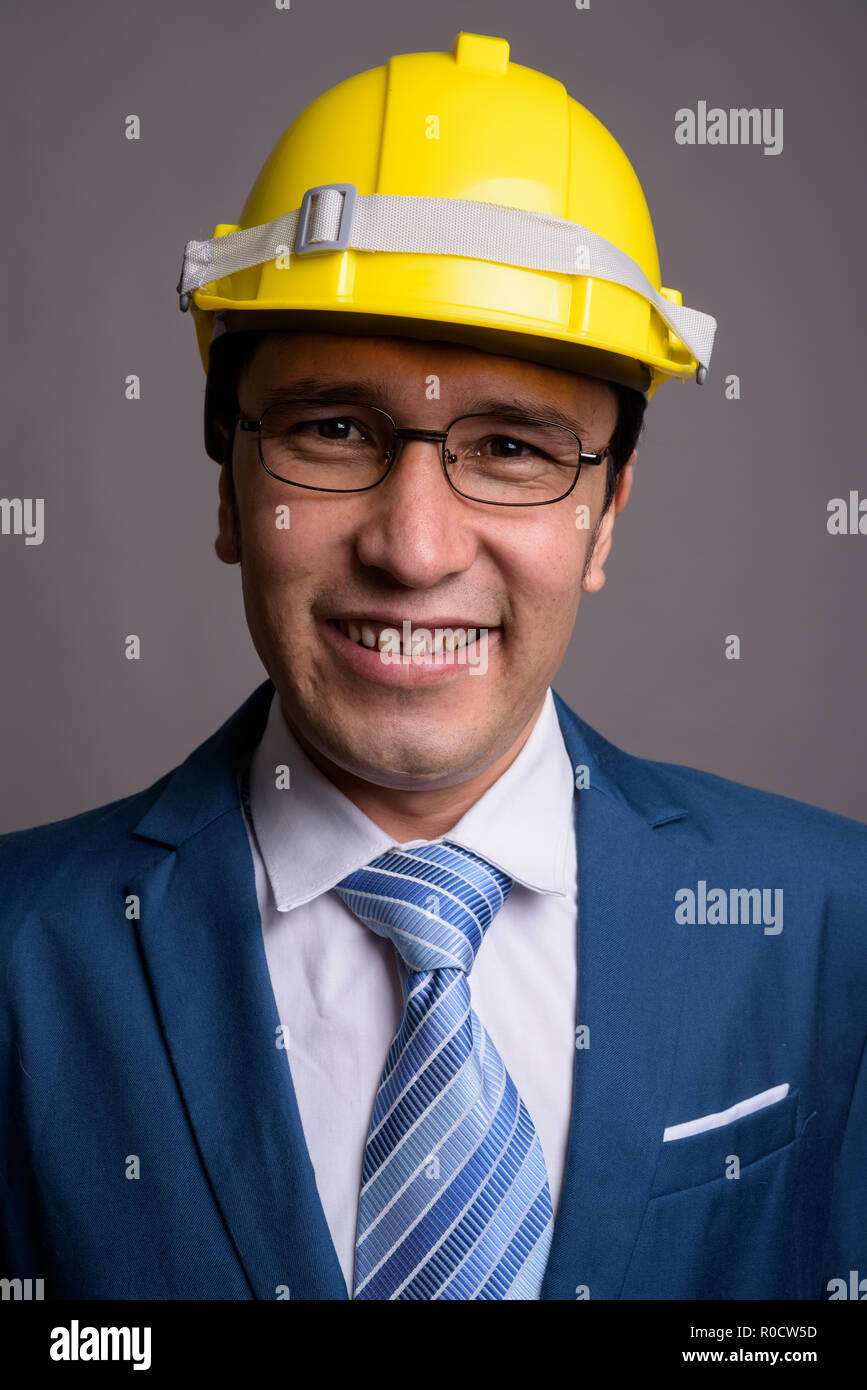 Young businessman wearing hardhat contre l'arrière-plan gris Banque D'Images